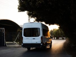 A white minivan drives on a quiet road under trees during a serene sunset.